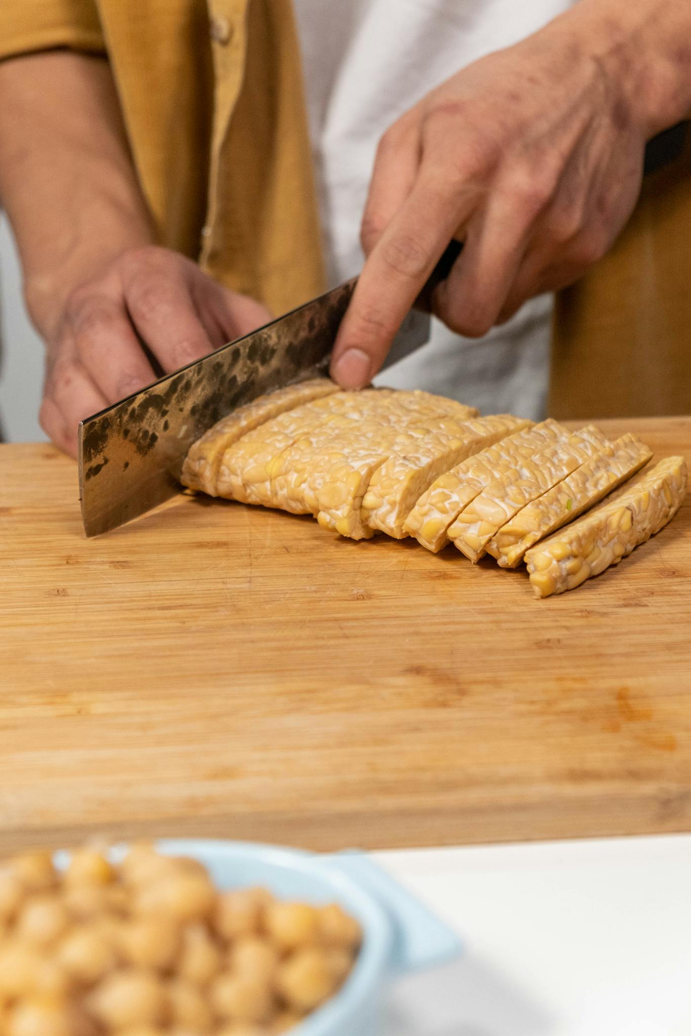 Close-up of hands slicing tempeh on a wooden board, ideal for vegan cooking themes.